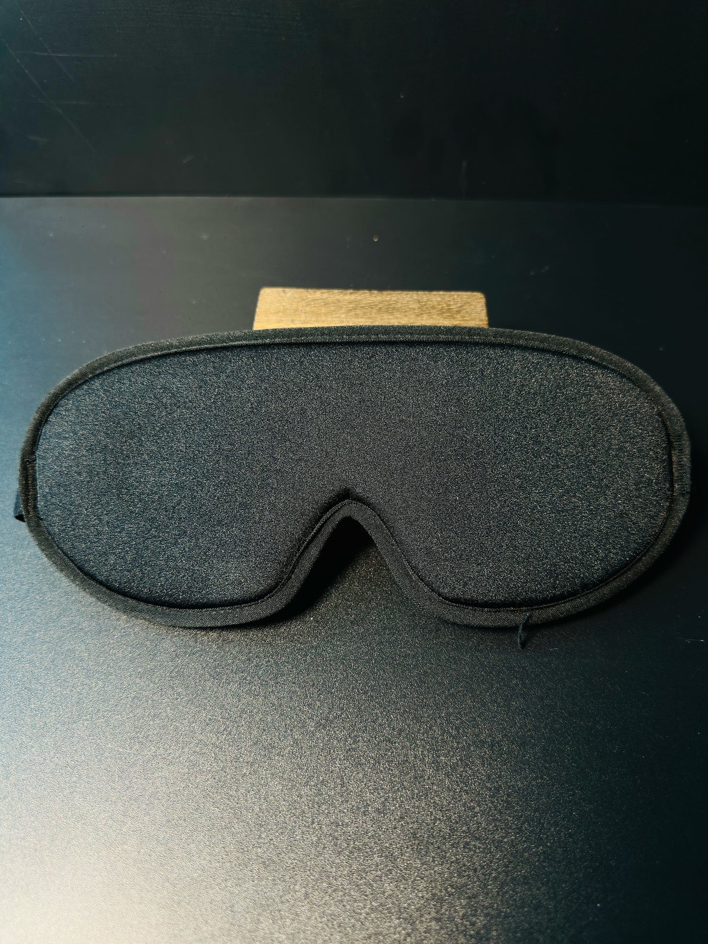 Black 3D sleep mask held in hand, showing its lightweight contoured shape and adjustable strap