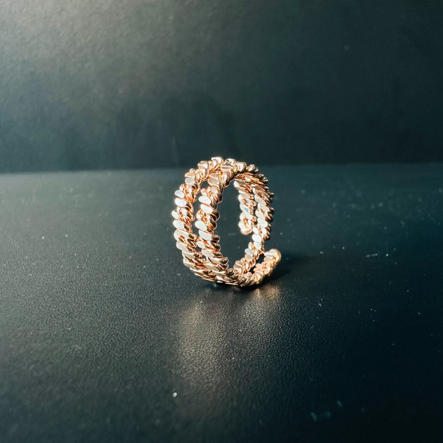 Handmade copper braided ring with two twisted rope bands and adjustable open back, on a dark surface