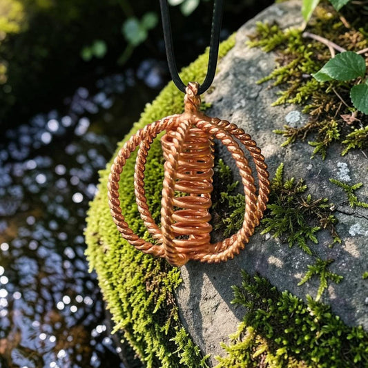 Copper tensor sphere pendant resting on moss outdoors, styled for meditation and mindful wear