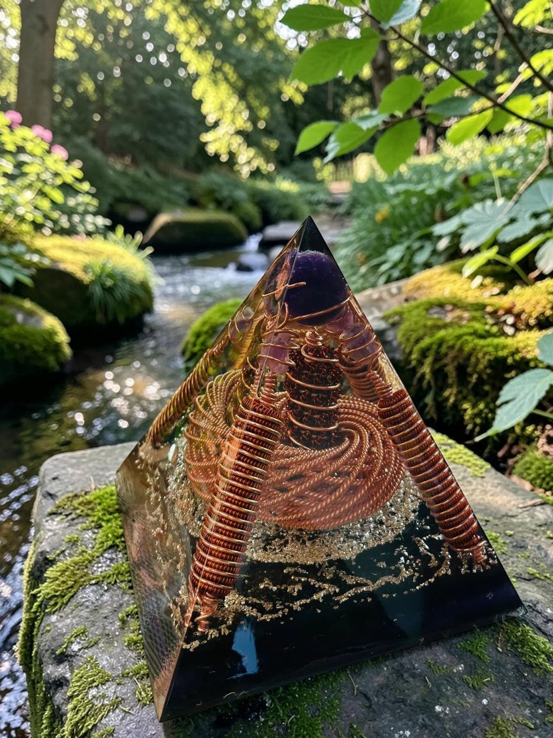 Kim tự tháp orgone abusta.viking bằng đồng nguyên chất xoắn, đá thạch anh tím, vàng lá, đặt trên đá phủ rêu bên suối.
