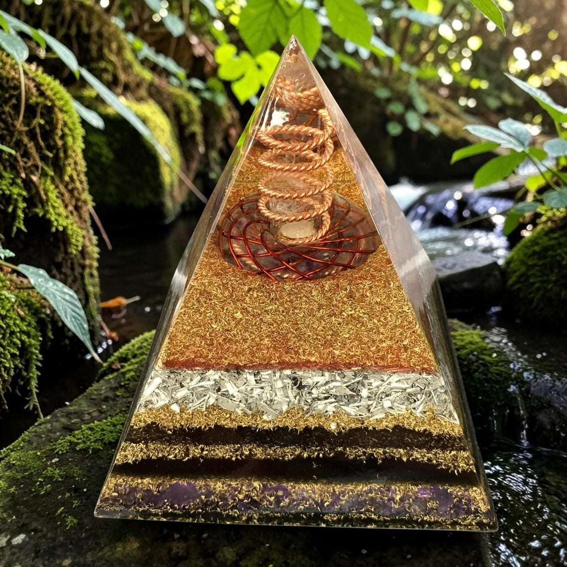 Tháp orgone bằng đồng abusta.viking, hình triskelion, đá thạch anh tím, kim loại và nhựa trong suốt, đặt ngoài trời gần suối.