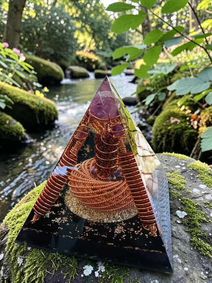 Tháp orgonite bằng đồng nguyên chất thủ công với đá thạch anh tím, đặt trên đá phủ rêu bên cạnh dòng suối.