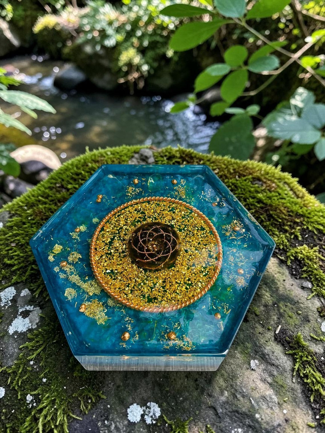 Tháp orgonite hình lục giác màu xanh ngọc bích, trang trí bằng vàng lá và đồng, có biểu tượng hoa sen ở giữa. abusta.viking