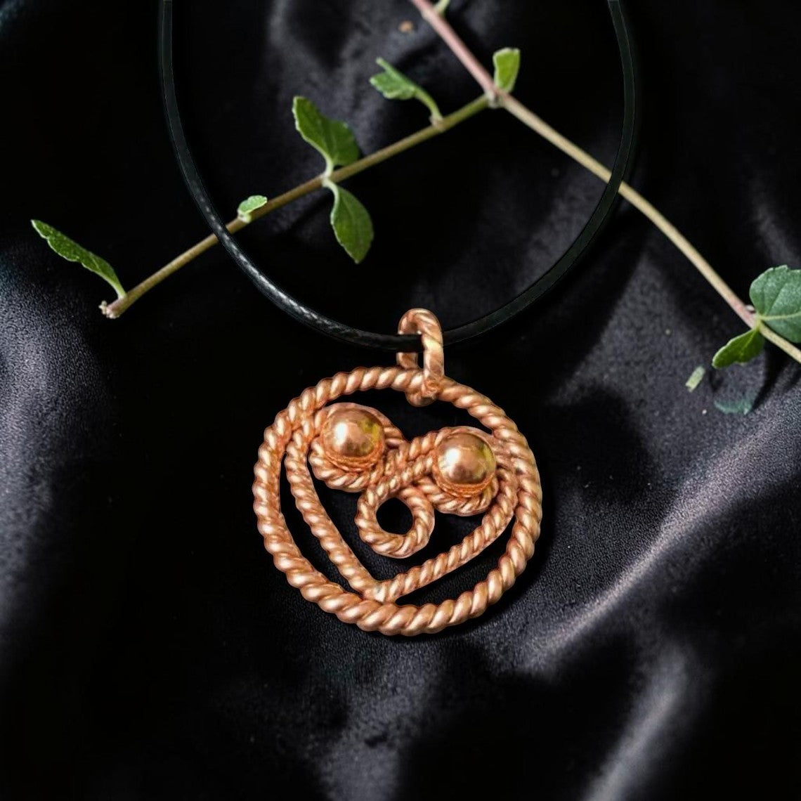 Con lắc đồng Tensor Sacred Pendulum Dowsing thủ công từ đồng nguyên chất, thiết kế hình trái tim xoắn với hai viên bi nhỏ, dây đeo đen, trên nền lụa đen.