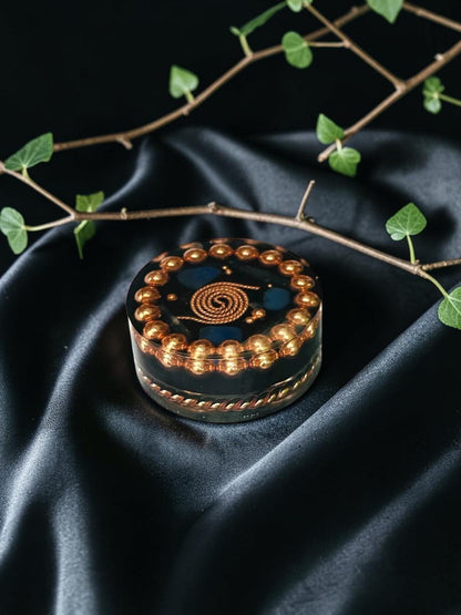 Đĩa sạc orgonite thủ công bằng đồng nguyên chất của abusta.viking, có hoa văn hình xoắn ốc bằng đồng và các viên đá màu xanh lam.