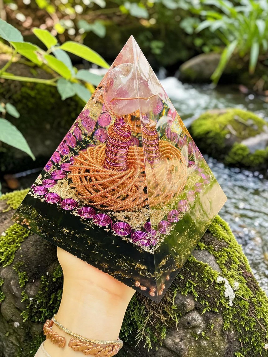 Tháp orgone abusta.viking bằng đồng nguyên chất xoắn kép, có đá thạch anh tím, trang trí lấp lánh, đặt trên đá phủ rêu bên suối.