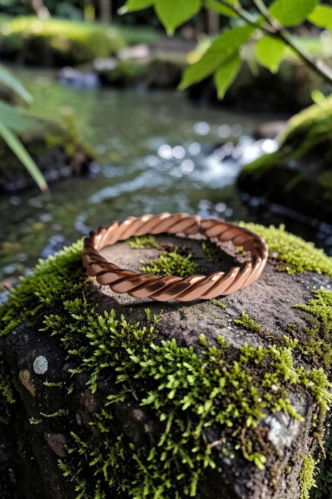Vòng đeo tay Abusta Viking bằng đồng nguyên chất, thủ công tinh xảo, thiết kế xoắn ốc, đặt trên đá phủ rêu bên suối.