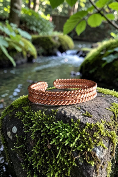 Vòng đeo tay bằng đồng nguyên chất abusta.viking, thiết kế xoắn kép, phong cách boho, đặt trên đá phủ rêu bên suối.