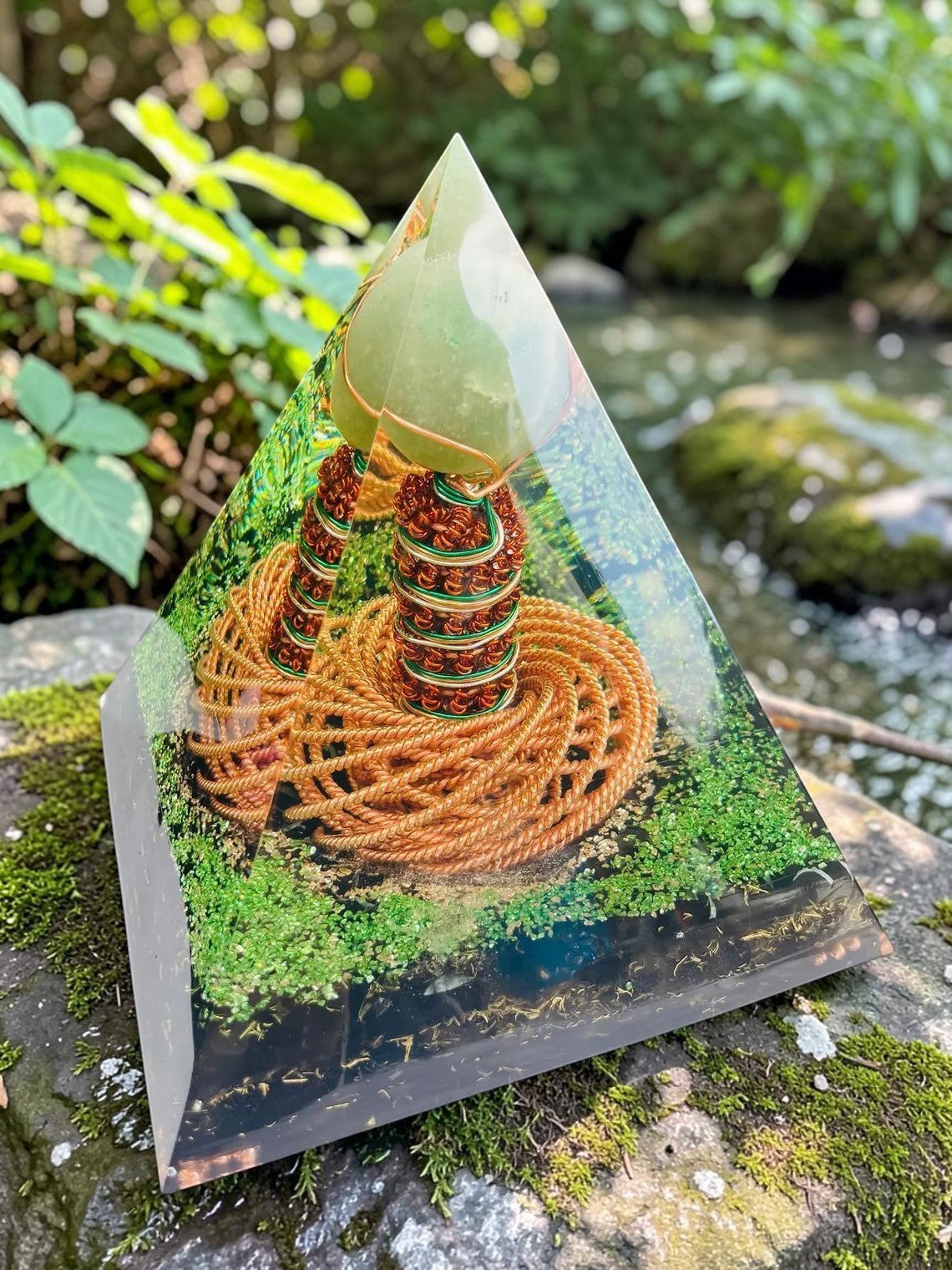 Kim tự tháp orgone abusta.viking với cuộn dây đồng xoắn kép và đá ngọc bích xanh lá cây bên trong, đặt trên đá phủ rêu.