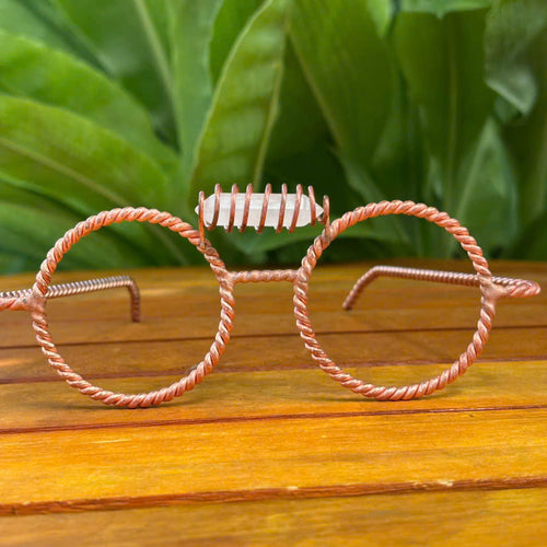 Handmade clear quartz copper tensor glasses with twisted round wire-frame rims, on a wooden surface with green leaves background