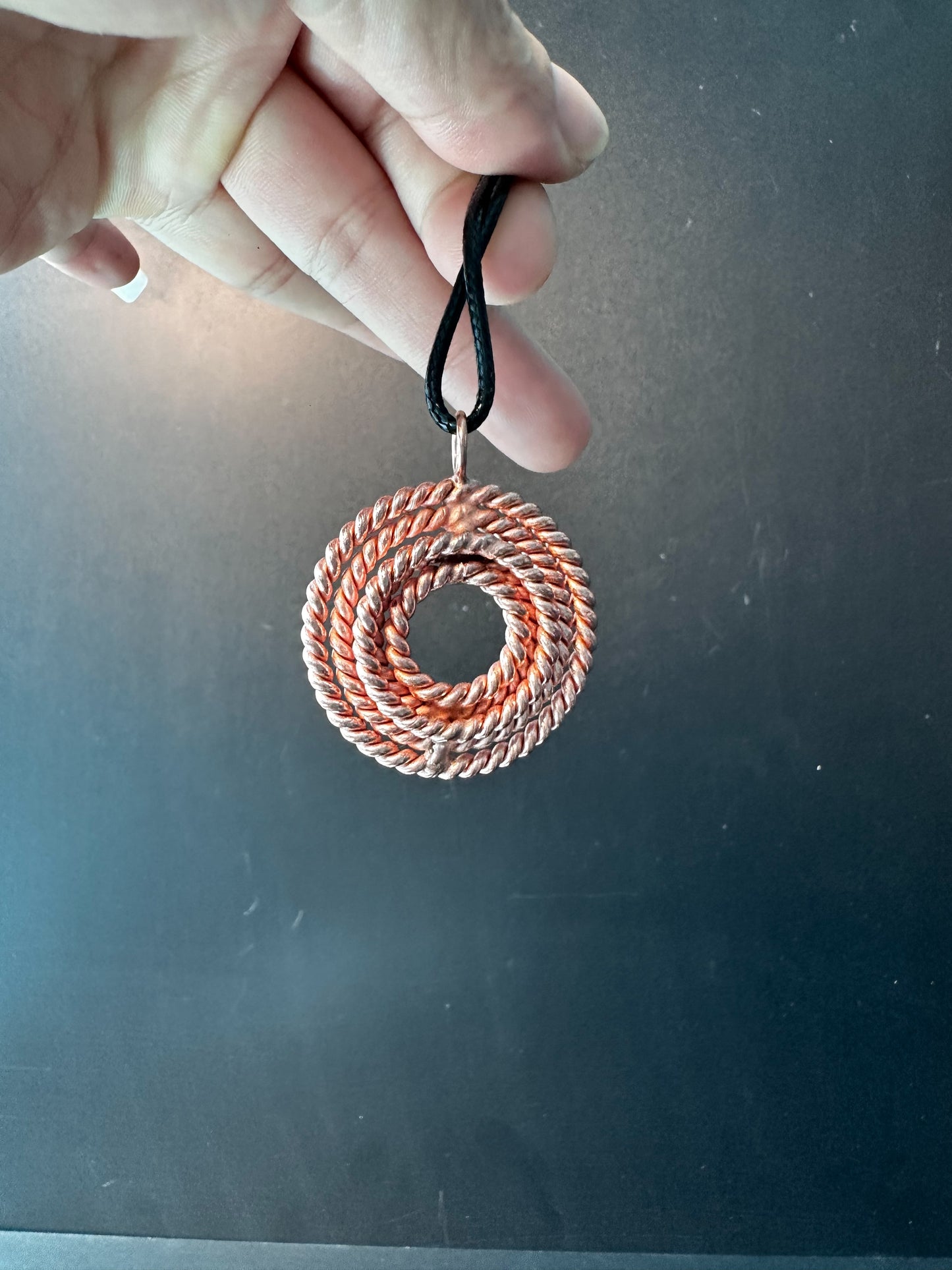 Copper five-frequency tensor pendant held by its black cord, showing the hand-woven concentric coil