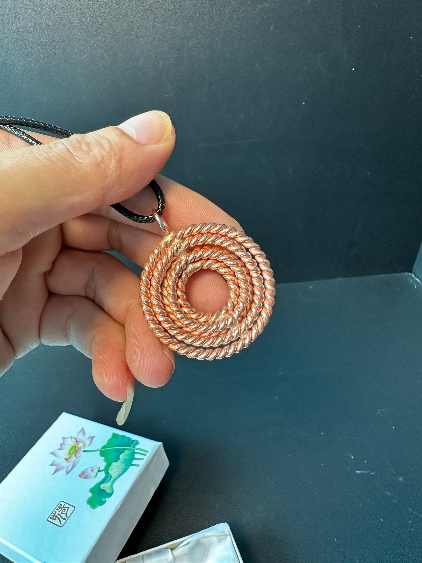 Copper sacred geometry pendant held in a hand for scale, a woven spiral tensor necklace in red copper