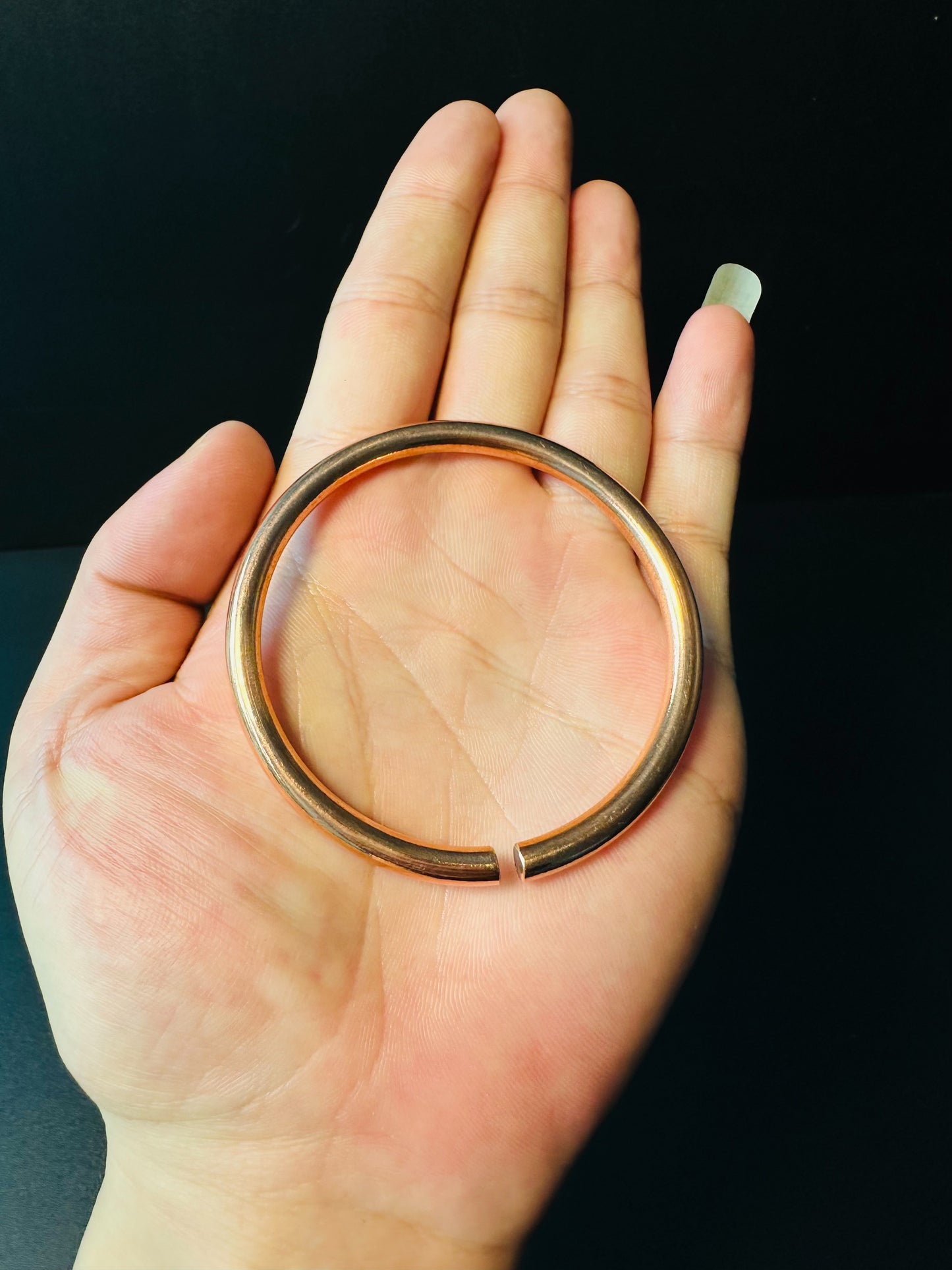 Copper bangle resting on a palm, showing its round shape and band thickness