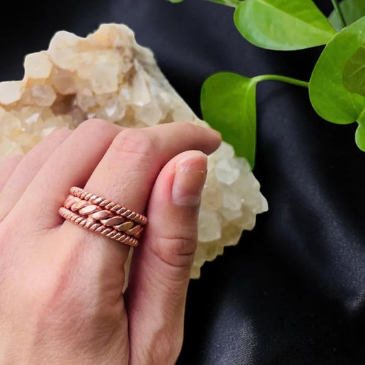 Copper Celtic trinity knot ring worn on a finger, resting on a quartz stone, handmade triquetra band