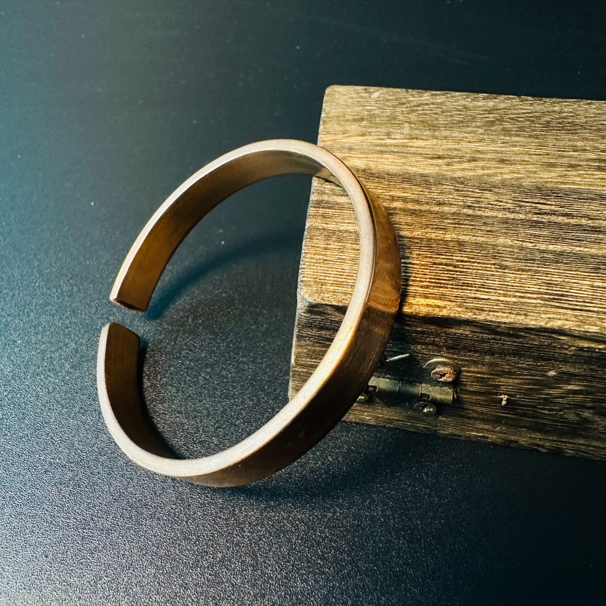 Handmade solid copper cuff bracelet with a smooth open design, leaning against rustic wood