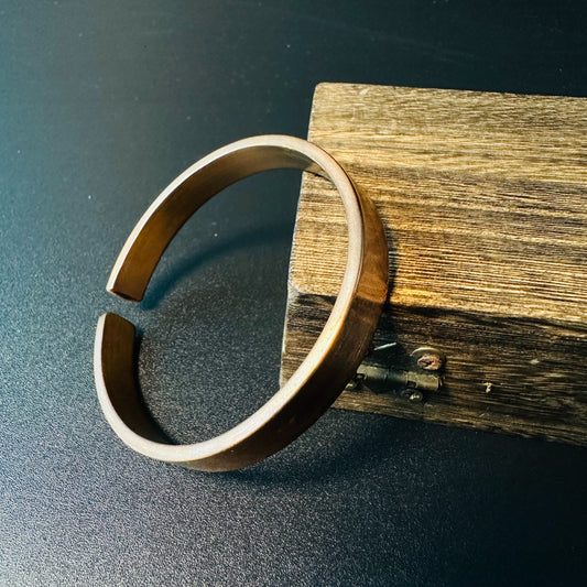 Handmade solid copper cuff bracelet with a smooth open design, leaning against rustic wood