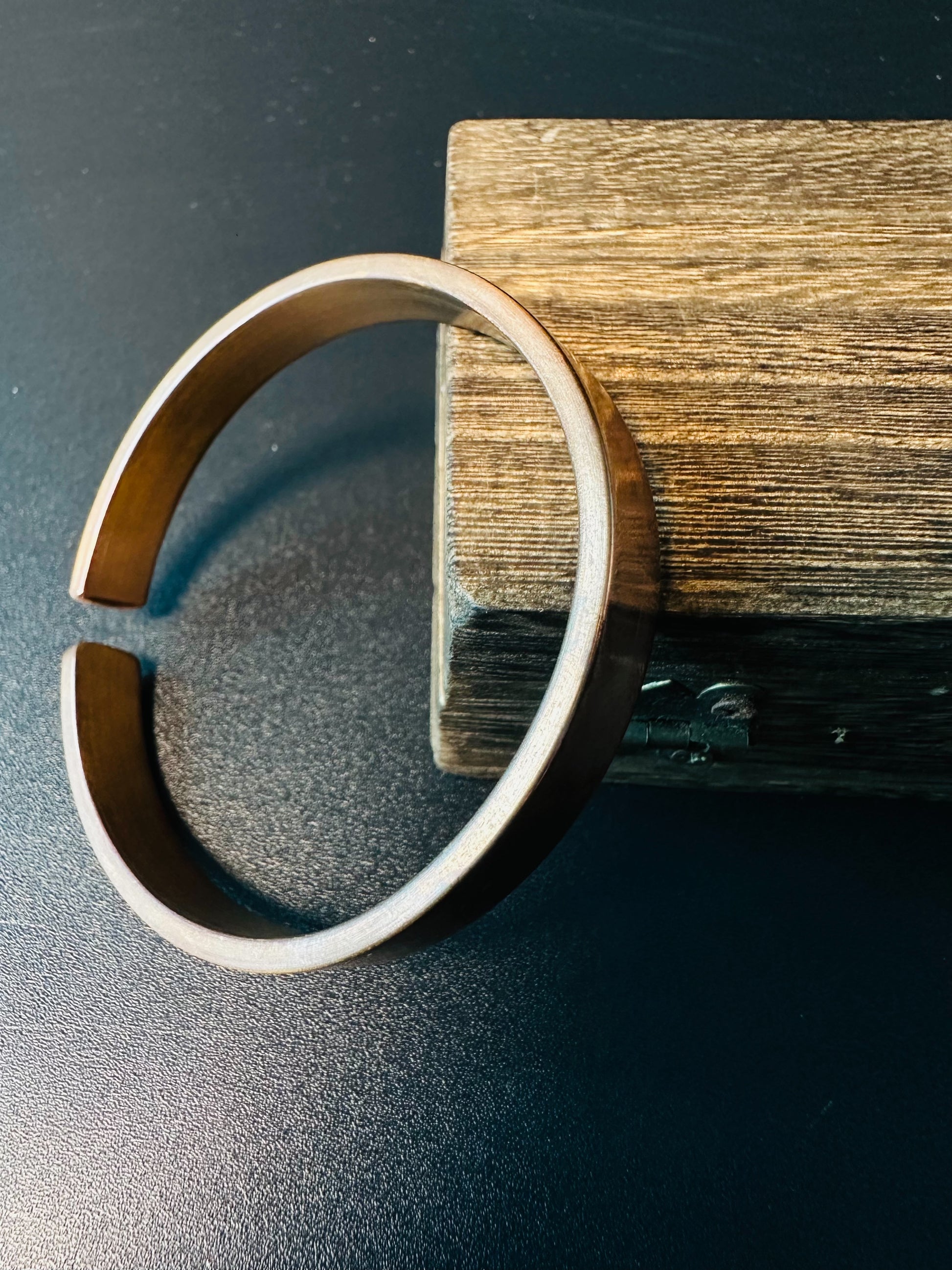 Side view of the open copper cuff bangle showing its flat band and warm brushed patina