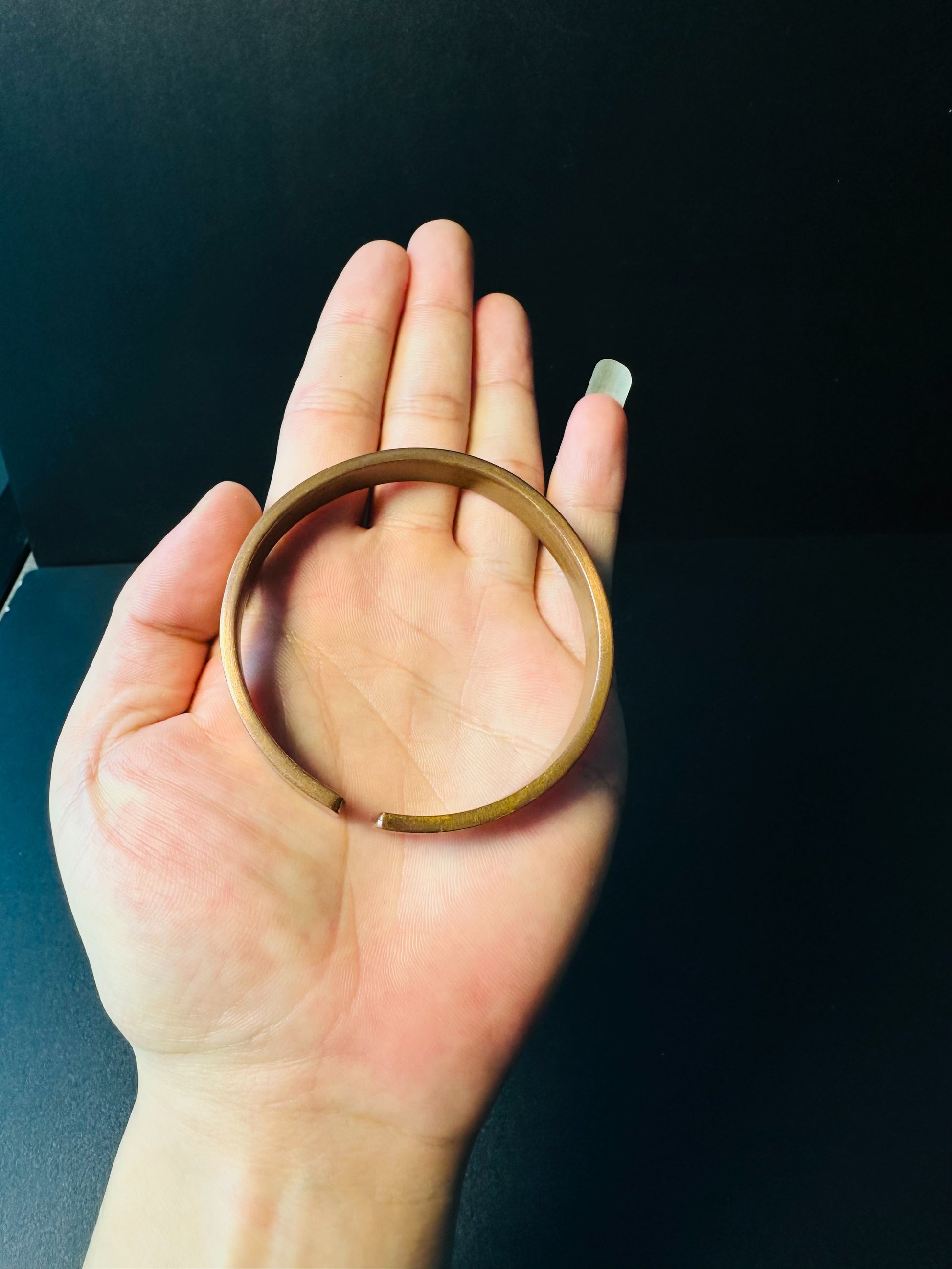 Copper cuff bracelet held in a palm, showing its wrist size and open back