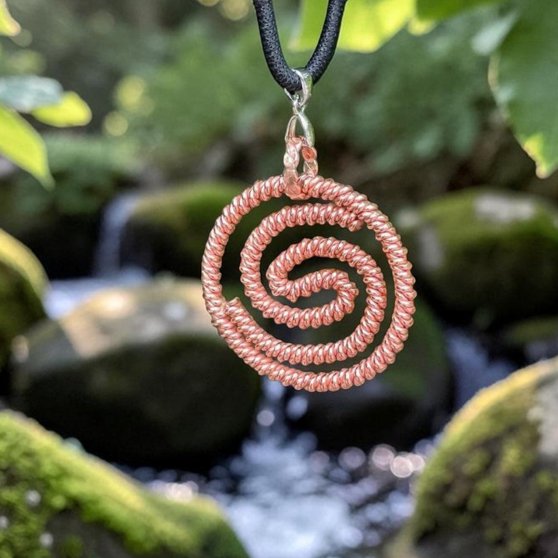 Copper double spiral pendant shaped to 144MHz, two hand-coiled spirals, hanging over a mossy rock
