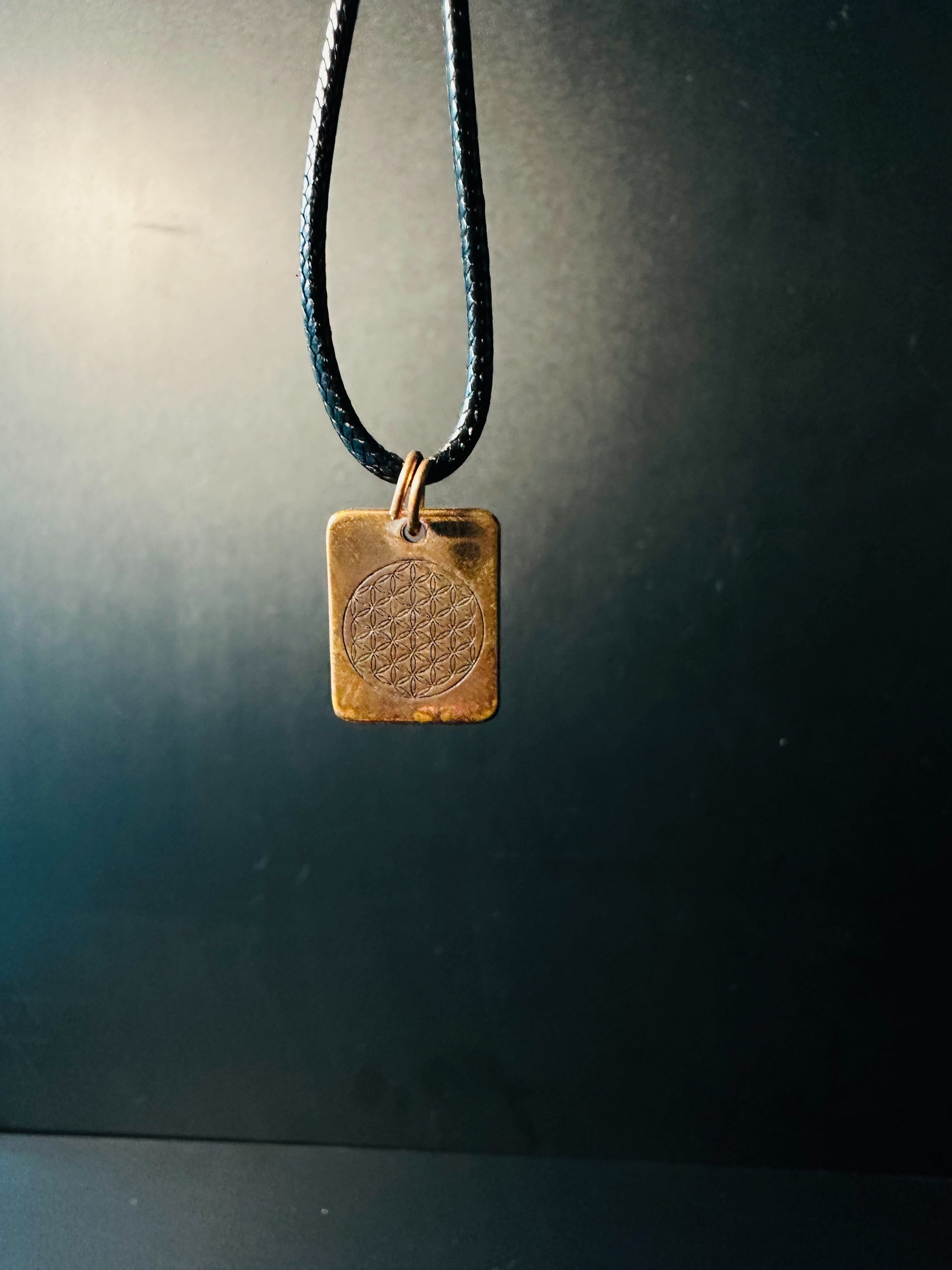 Copper Flower of Life pendant hanging from its adjustable cord, catching soft light