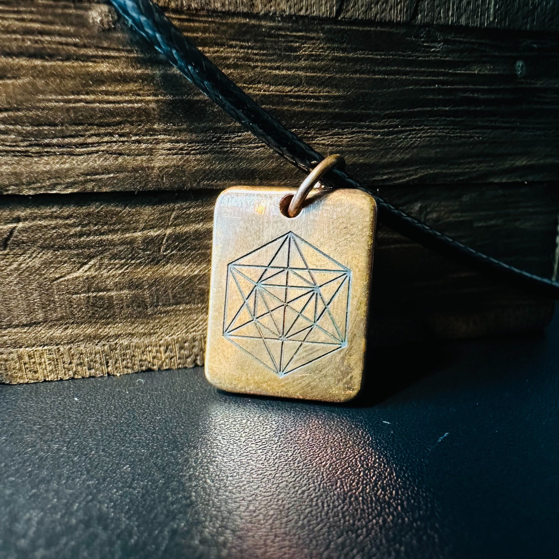 Handmade copper pendant engraved with Metatron's Cube sacred geometry, on a black cord against rustic wood