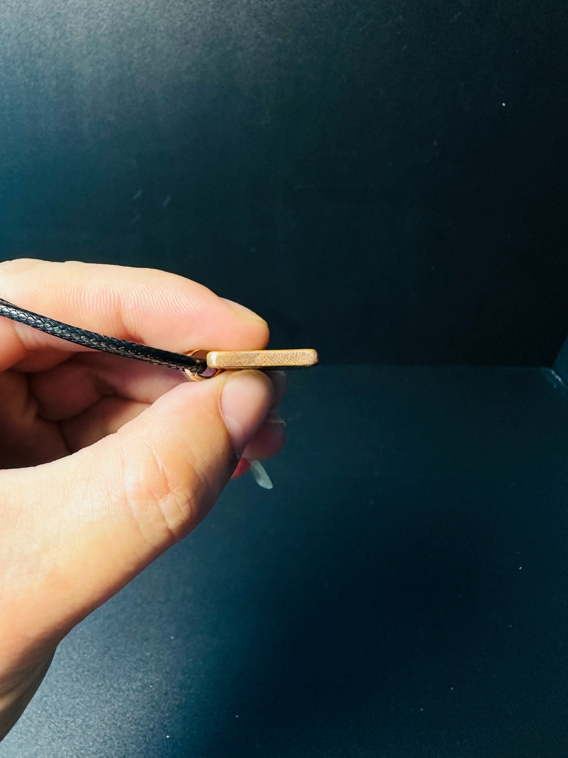 Side profile of the flat copper pendant showing its slim plate thickness and cord loop