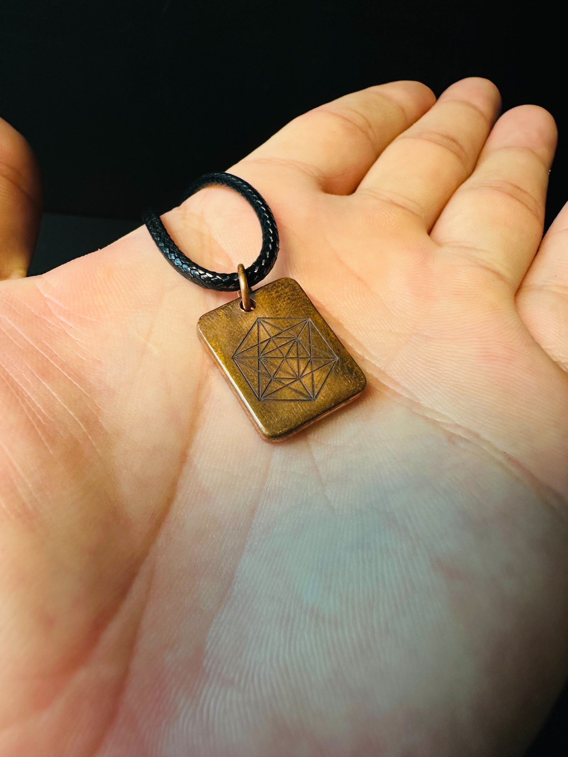 Copper sacred geometry pendant held in a palm, showing its compact everyday-wear size