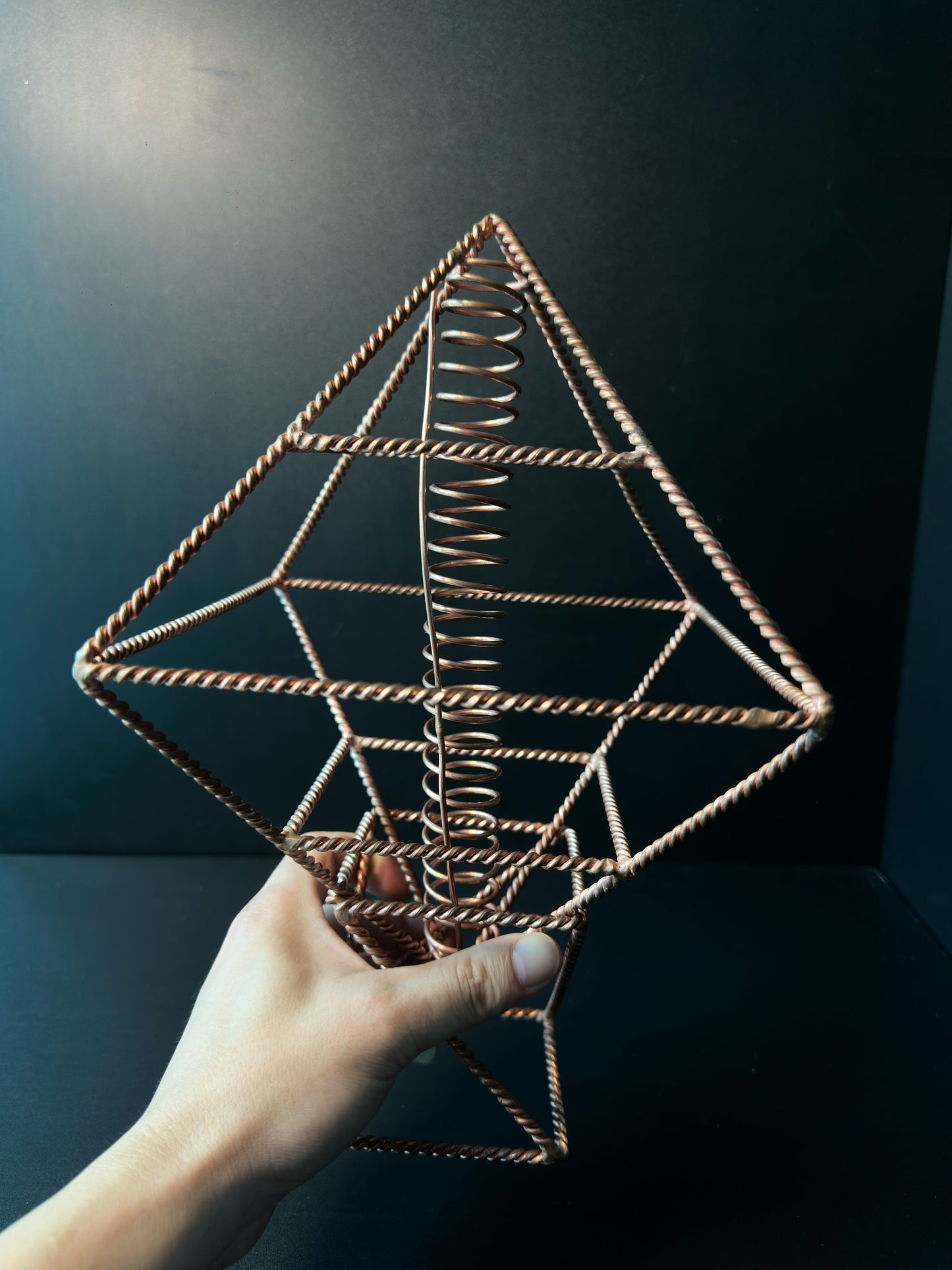 Copper sacred geometry octahedron held in hand, twisted wire energy tool with central coil