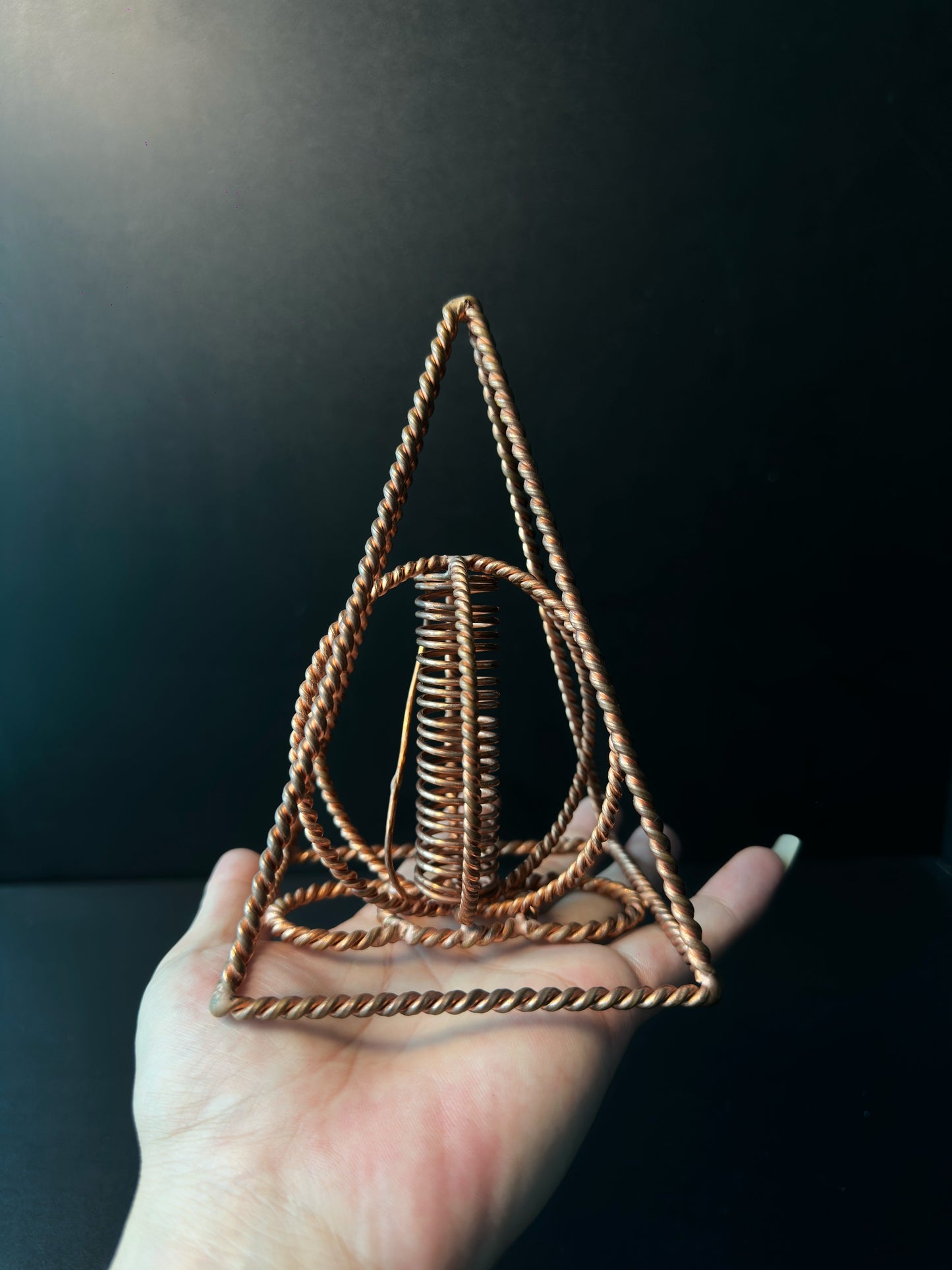 Palm-sized copper pyramid coil held in a hand, showing its scale and open frame