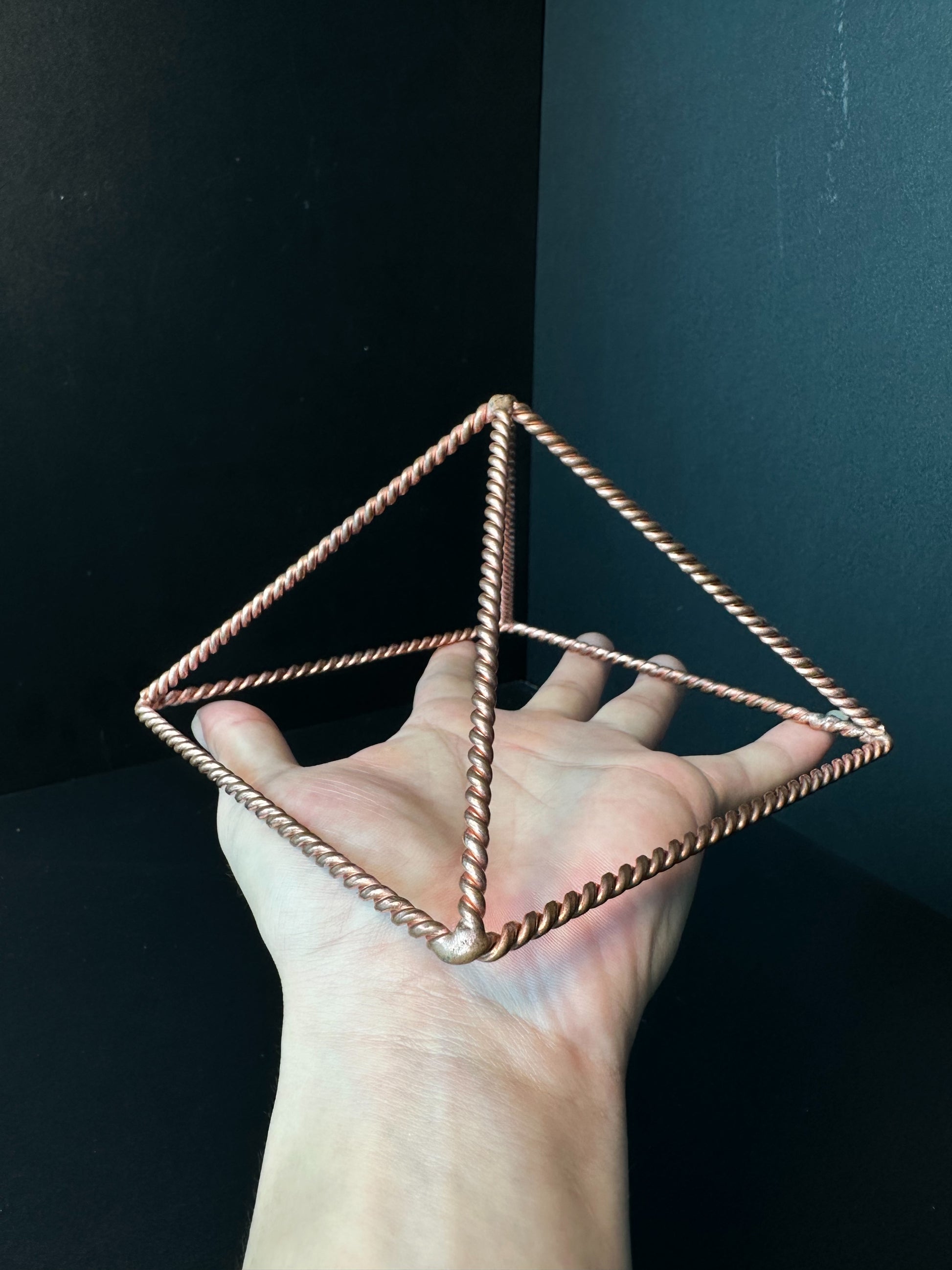 Large 23 cm copper pyramid frame held over a forearm for scale, open twisted-wire meditation pyramid