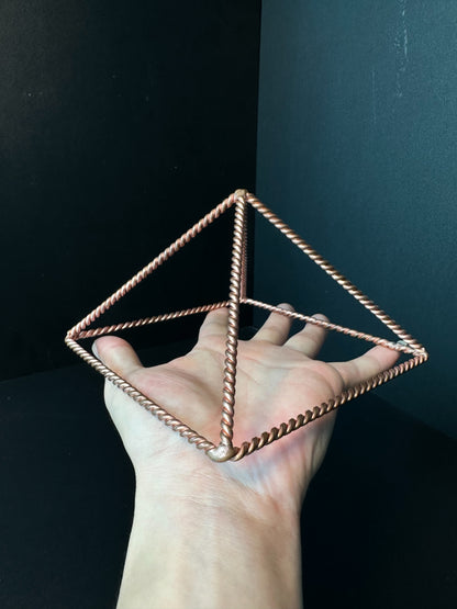 Large 23 cm copper pyramid frame held over a forearm for scale, open twisted-wire meditation pyramid