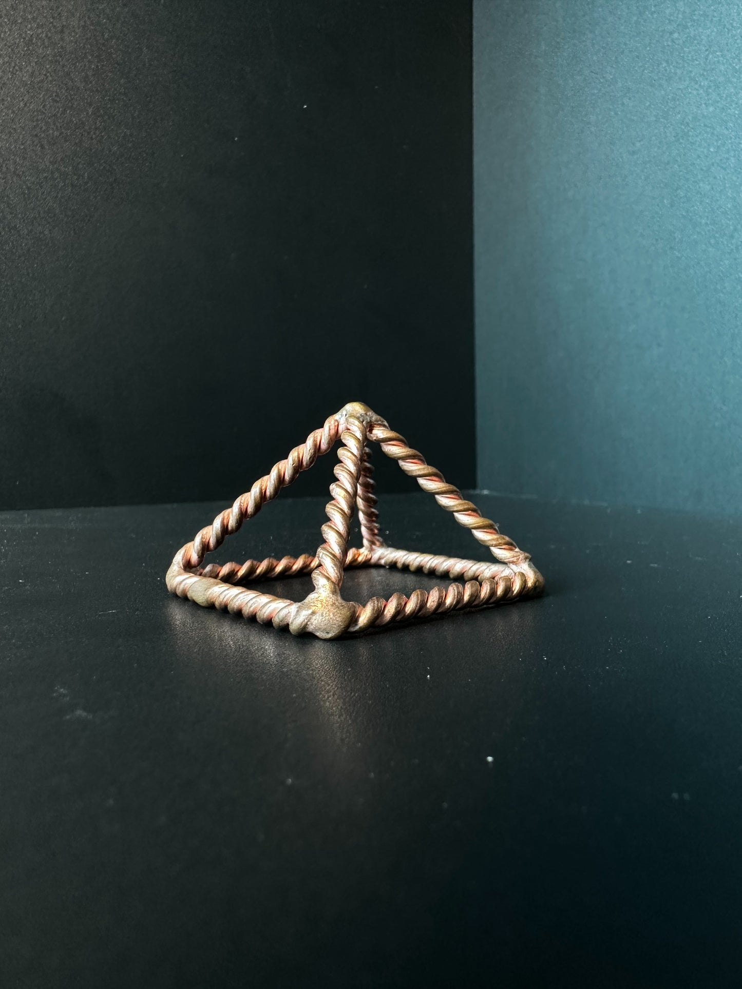 Set of five handmade copper pyramid frames in graduated sizes on a wooden table, twisted wire edges