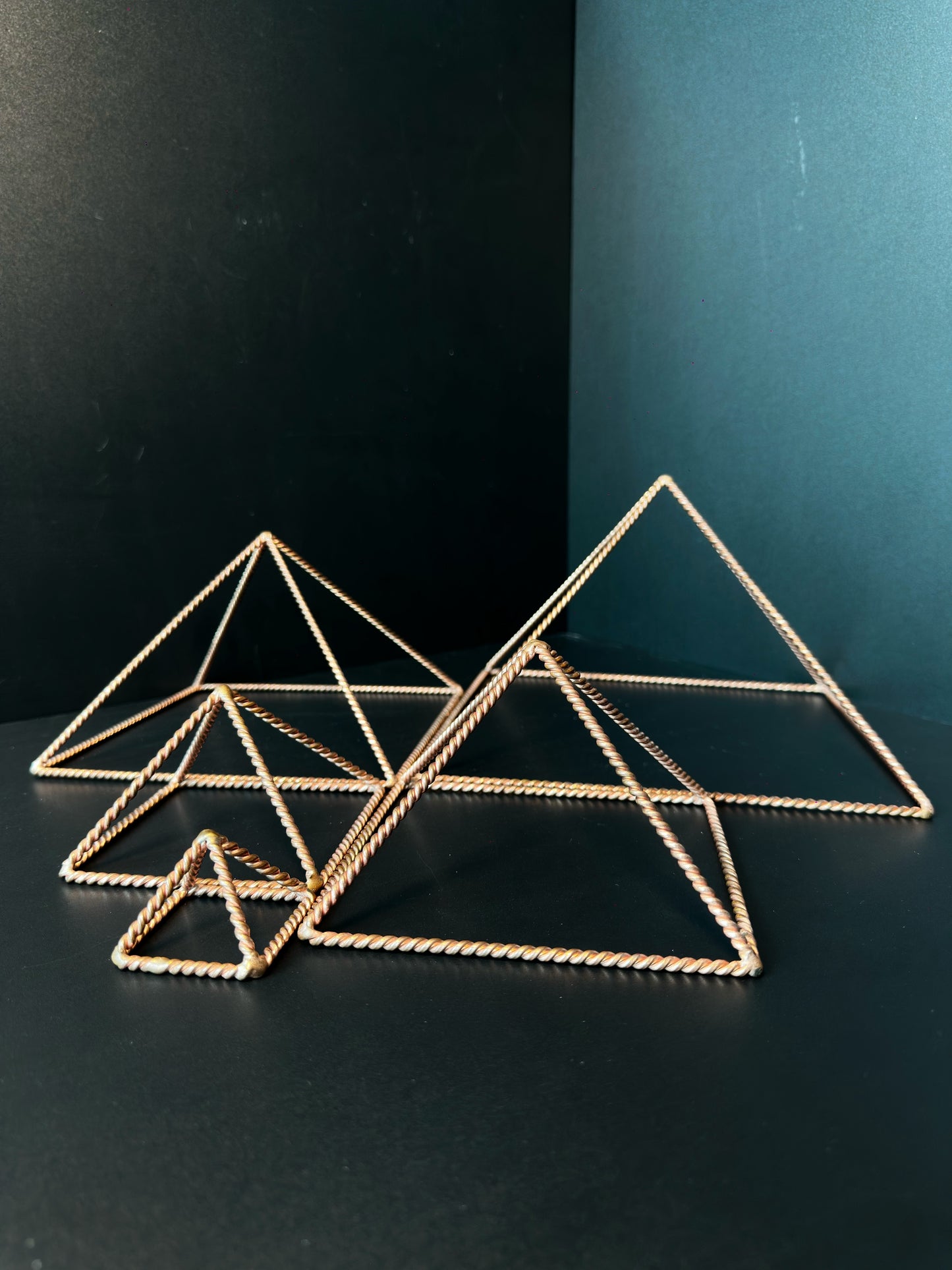 Handmade open copper pyramid frame in twisted wire on a dark surface