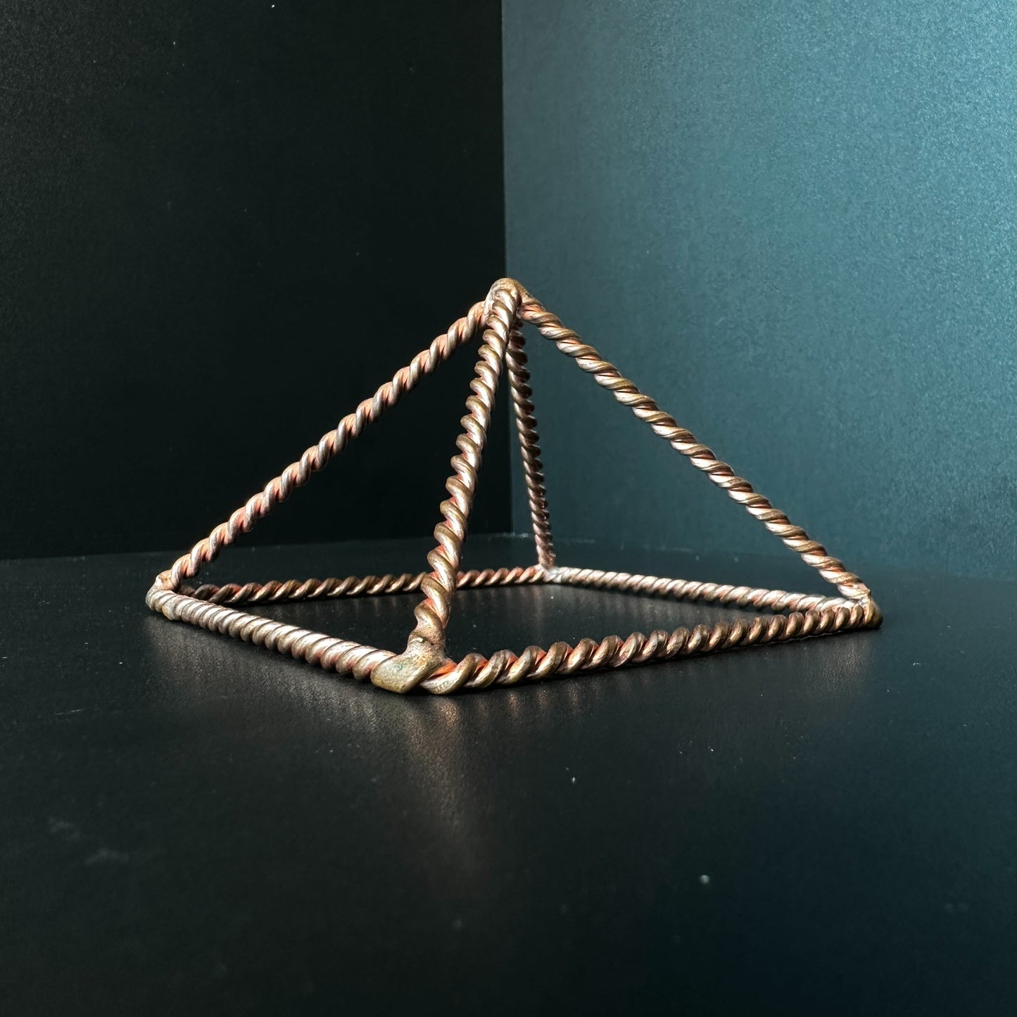 Handmade open copper pyramid frame in twisted wire on a dark surface