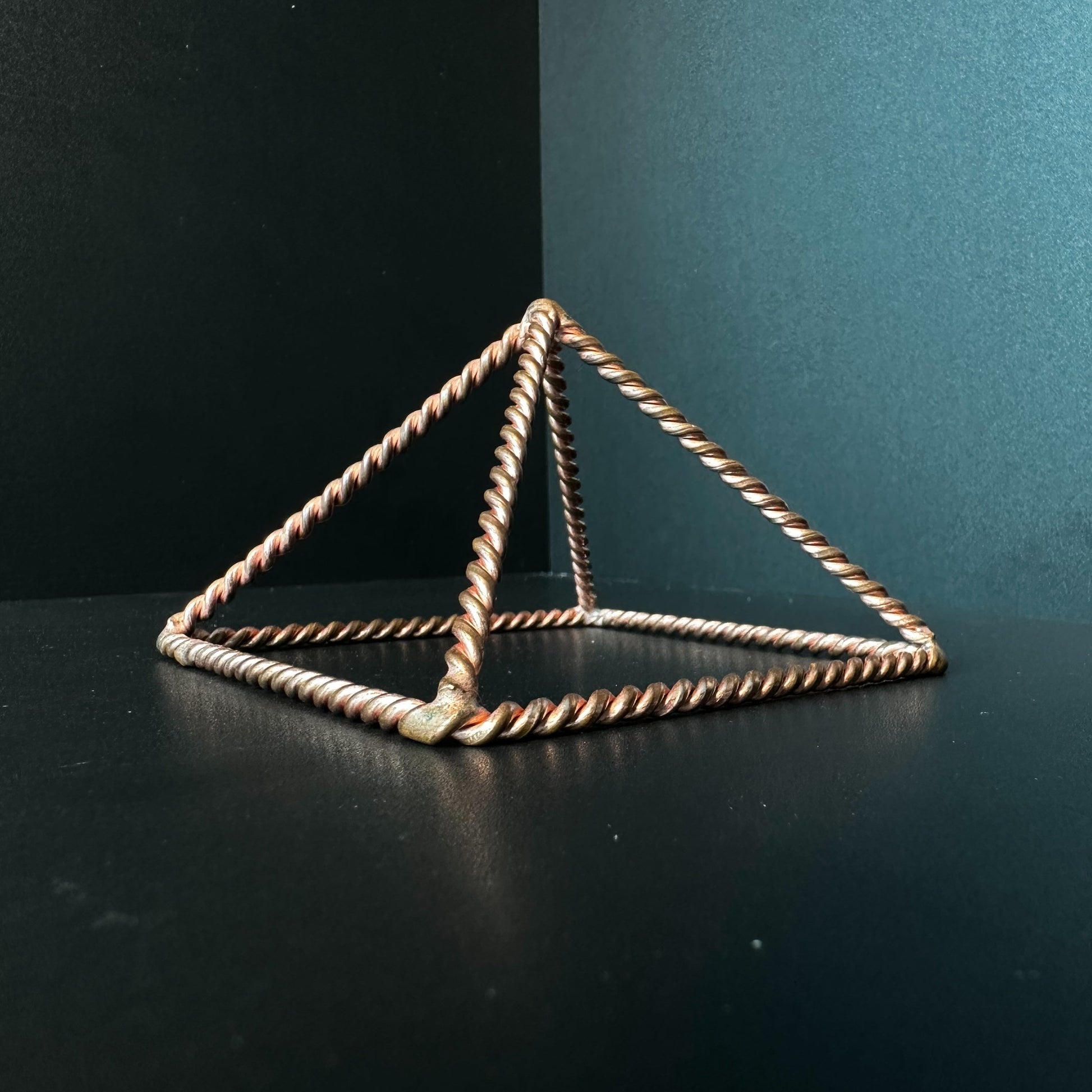 Handmade open copper pyramid frame in twisted wire on a dark surface
