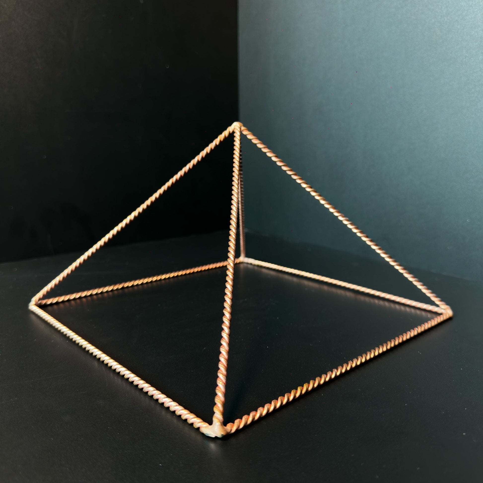 Handmade open copper pyramid frame in twisted wire on a dark surface