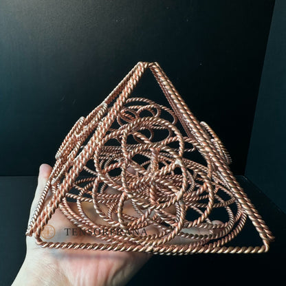 Copper pyramid held at an angle, showing its four woven sides rising to a point
