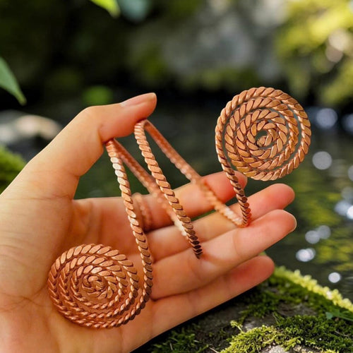 Handmade copper double-ended spiral coil held in an open hand, 188MHz Empowerment Cubit, by a stream