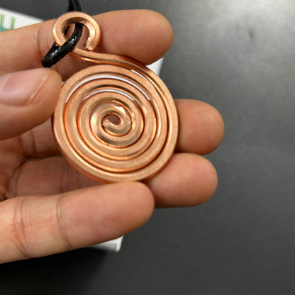 Handmade pure copper spiral coil pendant held in hand, minimalist vortex sacred geometry necklace showing spiral detail.