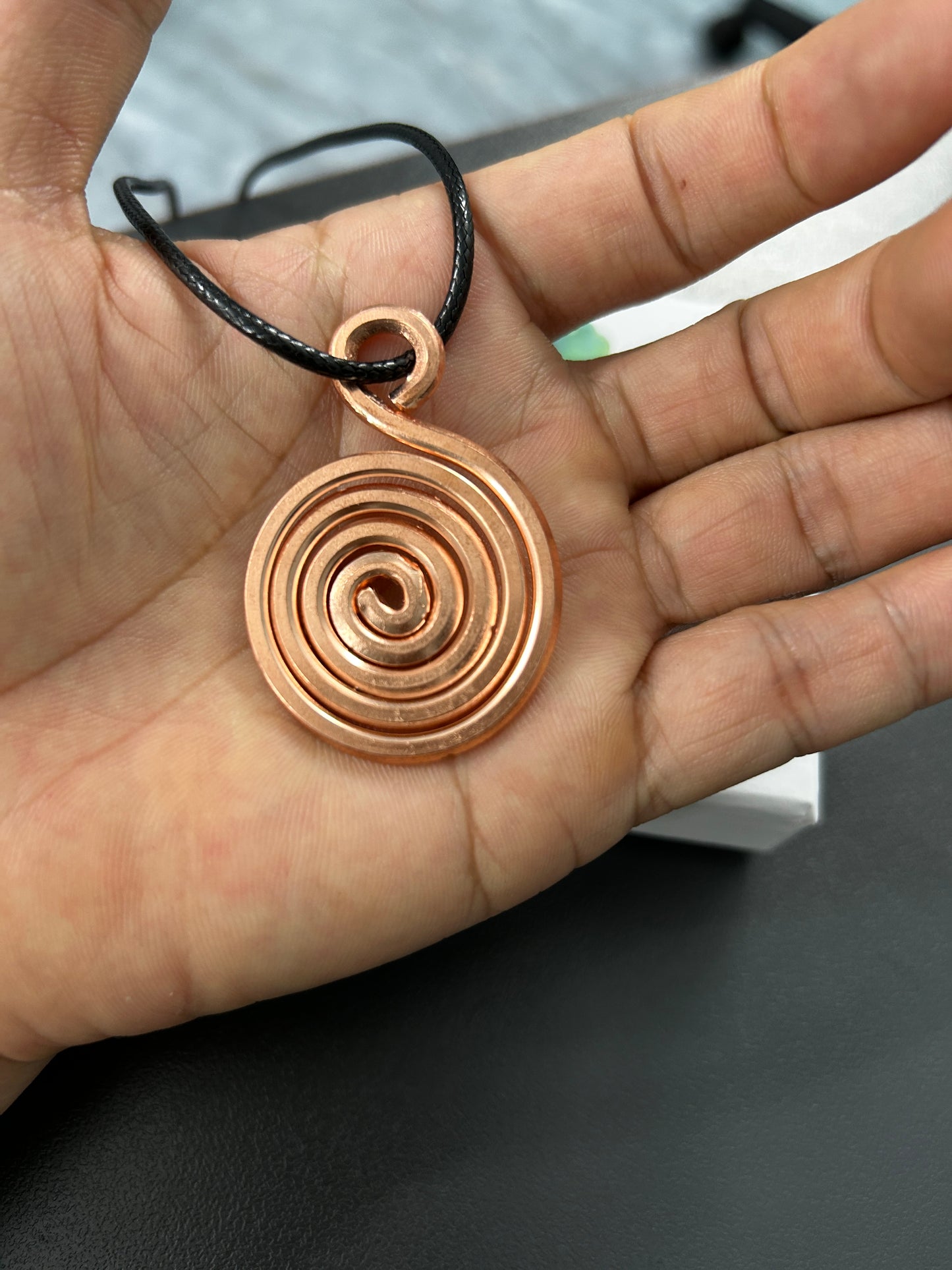 Copper spiral coil pendant held in palm, handmade unisex boho copper necklace on adjustable black cord.