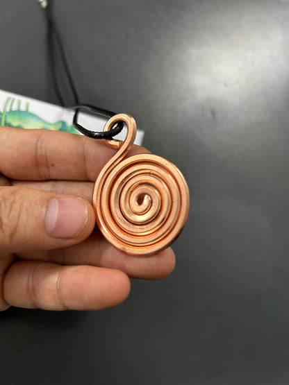 Side view of handmade copper spiral coil pendant showing bail and cord, solid pure copper vortex pendant.