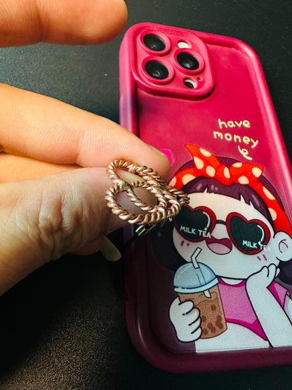 Twisted copper heart charm held between fingers beside a phone, showing handmade wire detail