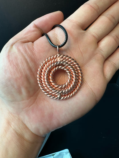 Woven copper tensor pendant resting on an open palm, close view of the spiral sacred geometry detail