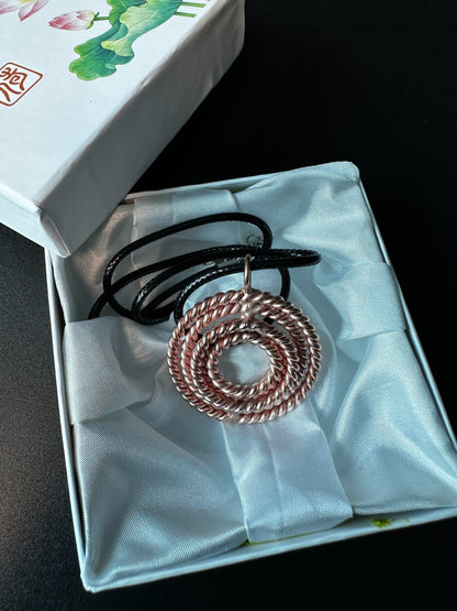 Copper tensor pendant with its black cord coiled on a soft pouch, handmade woven sacred geometry piece