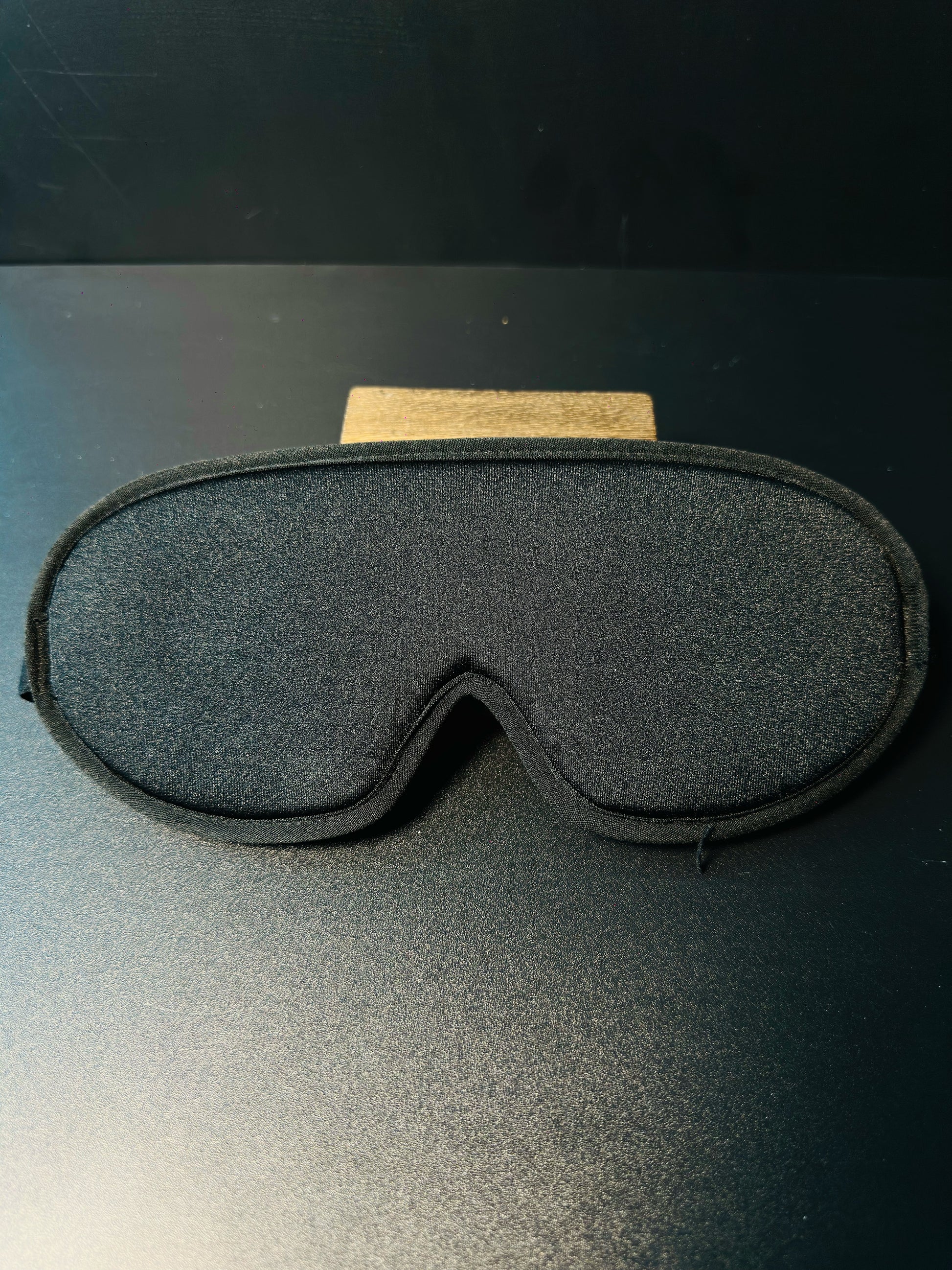 Black 3D sleep mask held in hand, showing its lightweight contoured shape and adjustable strap