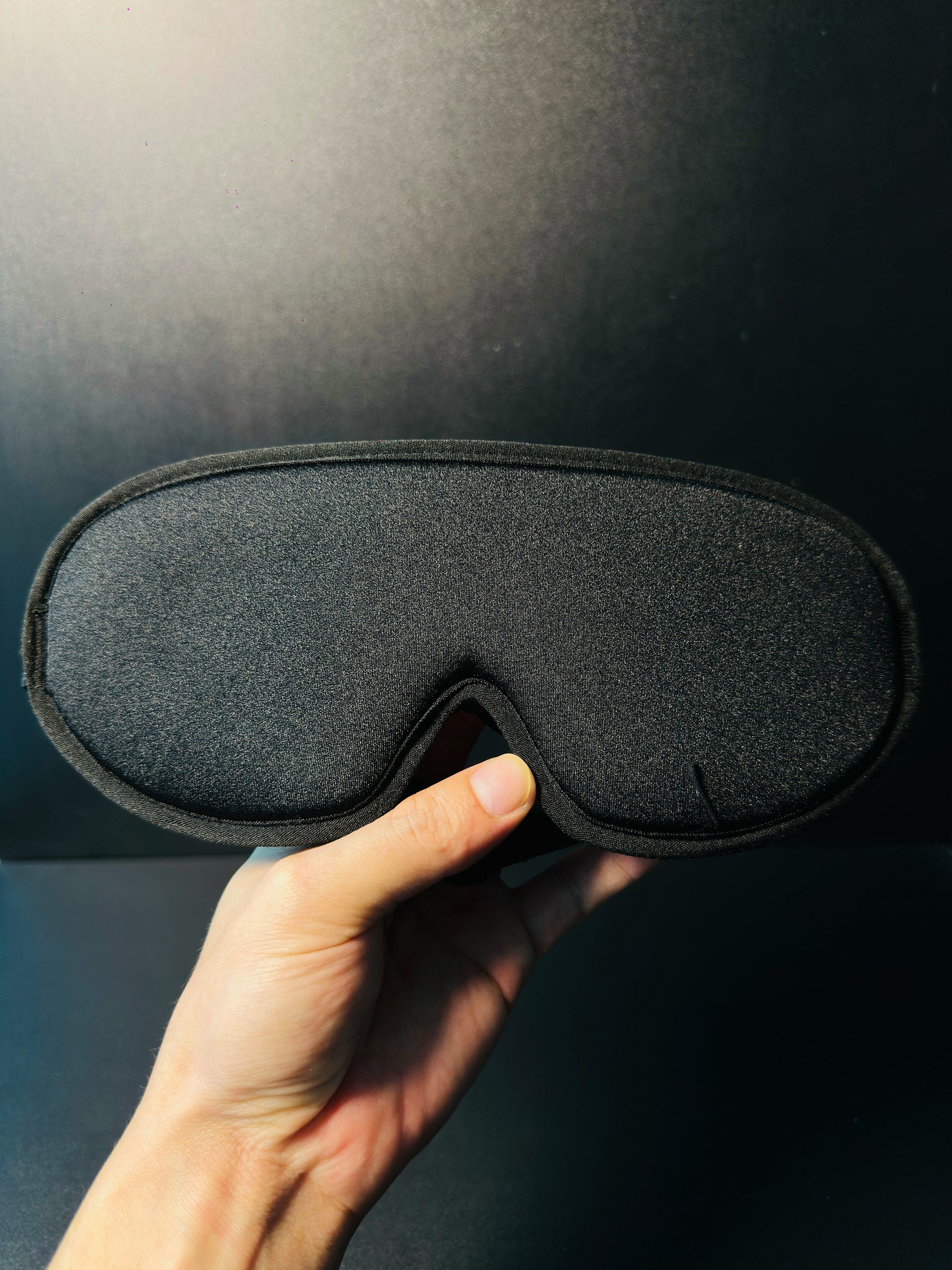 Hand holding the meditation eye mask, showing the twisted copper tensor rings inside the padded eye cavities