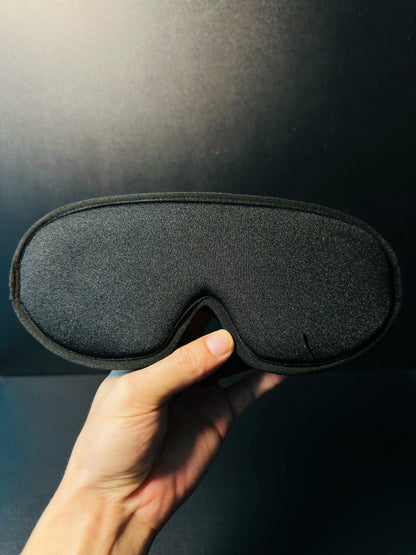 Hand holding the meditation eye mask, showing the twisted copper tensor rings inside the padded eye cavities