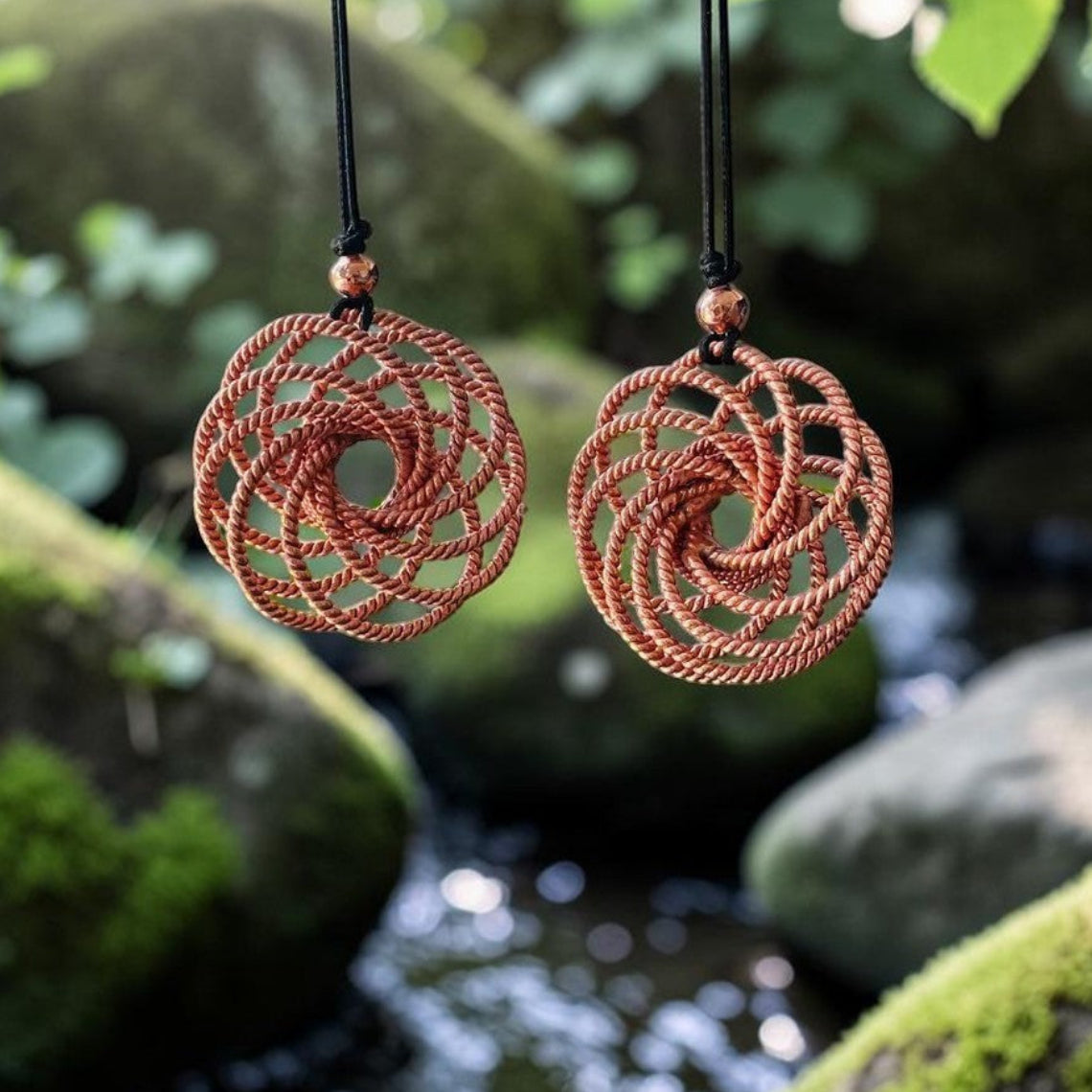 Copper tensor sphere water charger resting on stone by flowing water, handmade sacred geometry piece