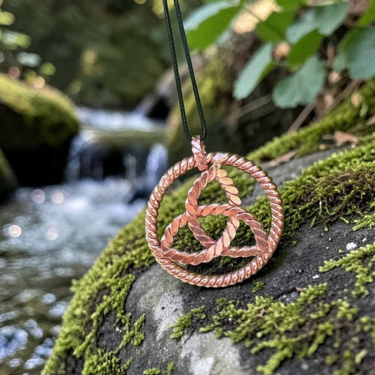 Copper triquetra pendant on a cord, three interlaced arcs in a circle, hanging over a mossy rock