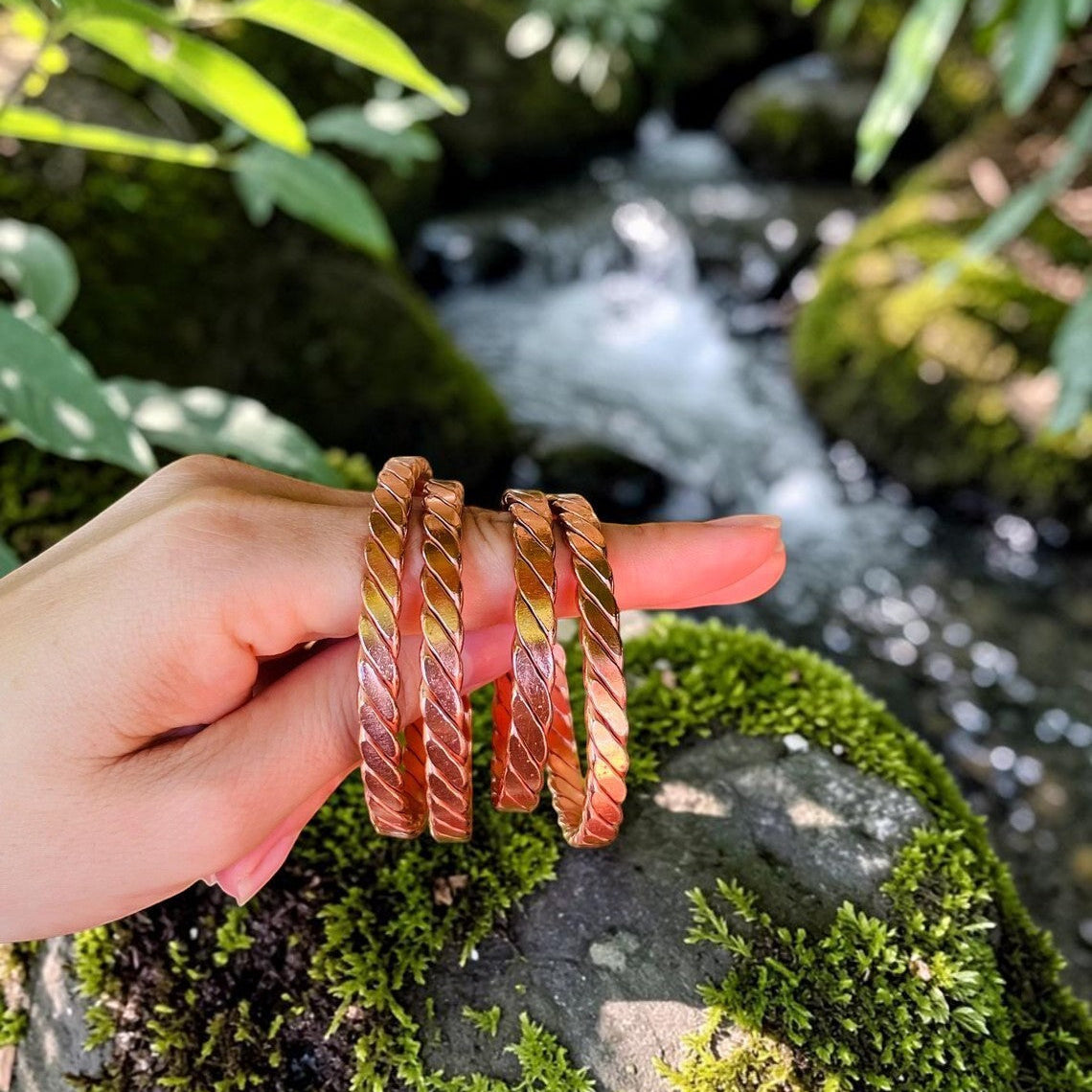 Handmade copper twisted bangle, a rope-twisted open cuff on a rock by a stream